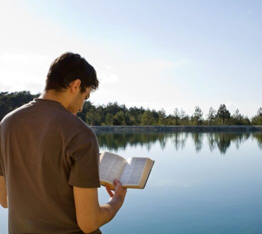 Young man in front of lake reading the Bible